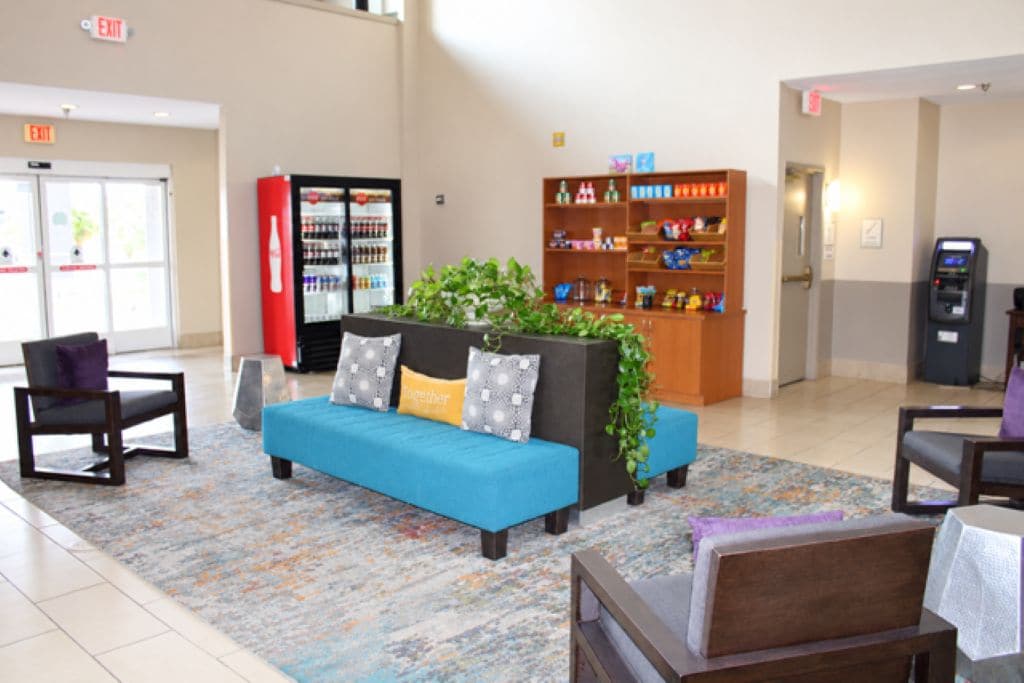 A lobby with a blue sofa, a red refrigerator, a bookshelf, and a vending machine.