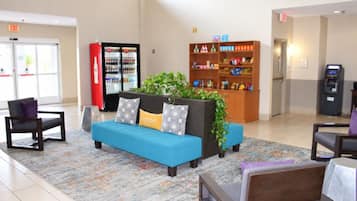 A lobby with a blue sofa, a red refrigerator, a bookshelf, and a vending machine.