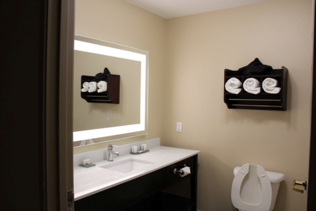 A bathroom with a double sink, a mirror, a towel rack, and a toilet.
