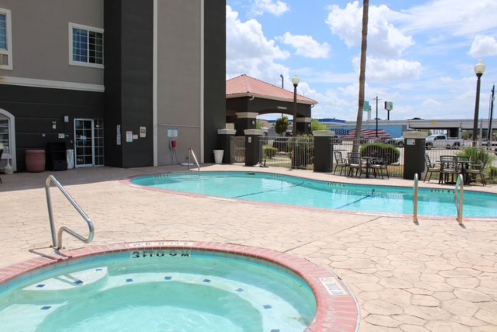 A hotel swimming pool area with a hot tub, outdoor seating, and a covered patio.