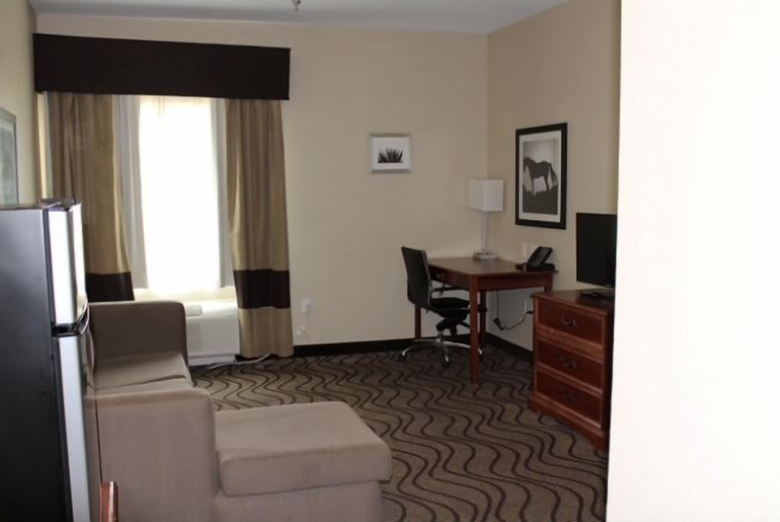 A hotel room with a bed, a desk, a chair, a television, and a dresser.