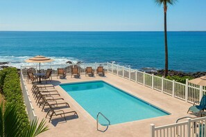 Un espace aménagé au bord de la piscine, avec des chaises, une table et une vue sur l’océan.