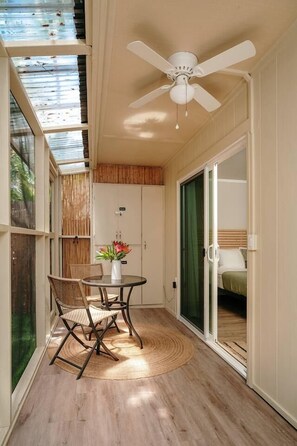 Une pièce dotée d’un ventilateur de plafond, d’une table à manger avec des chaises, d’une petite plante en pot et d’une porte-fenêtre coulissante donnant sur une chambre.