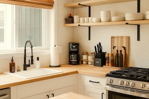 A kitchen with a modern stove, a coffee maker, and a sink with a black faucet. - The Alani at Kona Shores (Kailua-Kona)