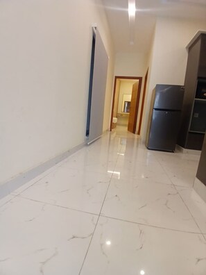 A hallway with a shiny tiled floor, a refrigerator, and a door leading to another room. - Tranquil 1-bedroom apartment with AC in welcoming Lahore (Lahore)
