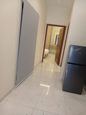A hallway with a refrigerator, a door, and a bathroom visible in the distance.