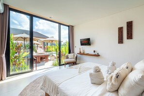 Un dormitorio con un gran ventanal corredero que da a un patio con mobiliario exterior y plantas.