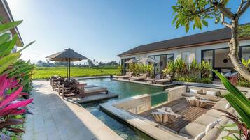 A pool area with lounge chairs, a small pool, and a view of a green field.