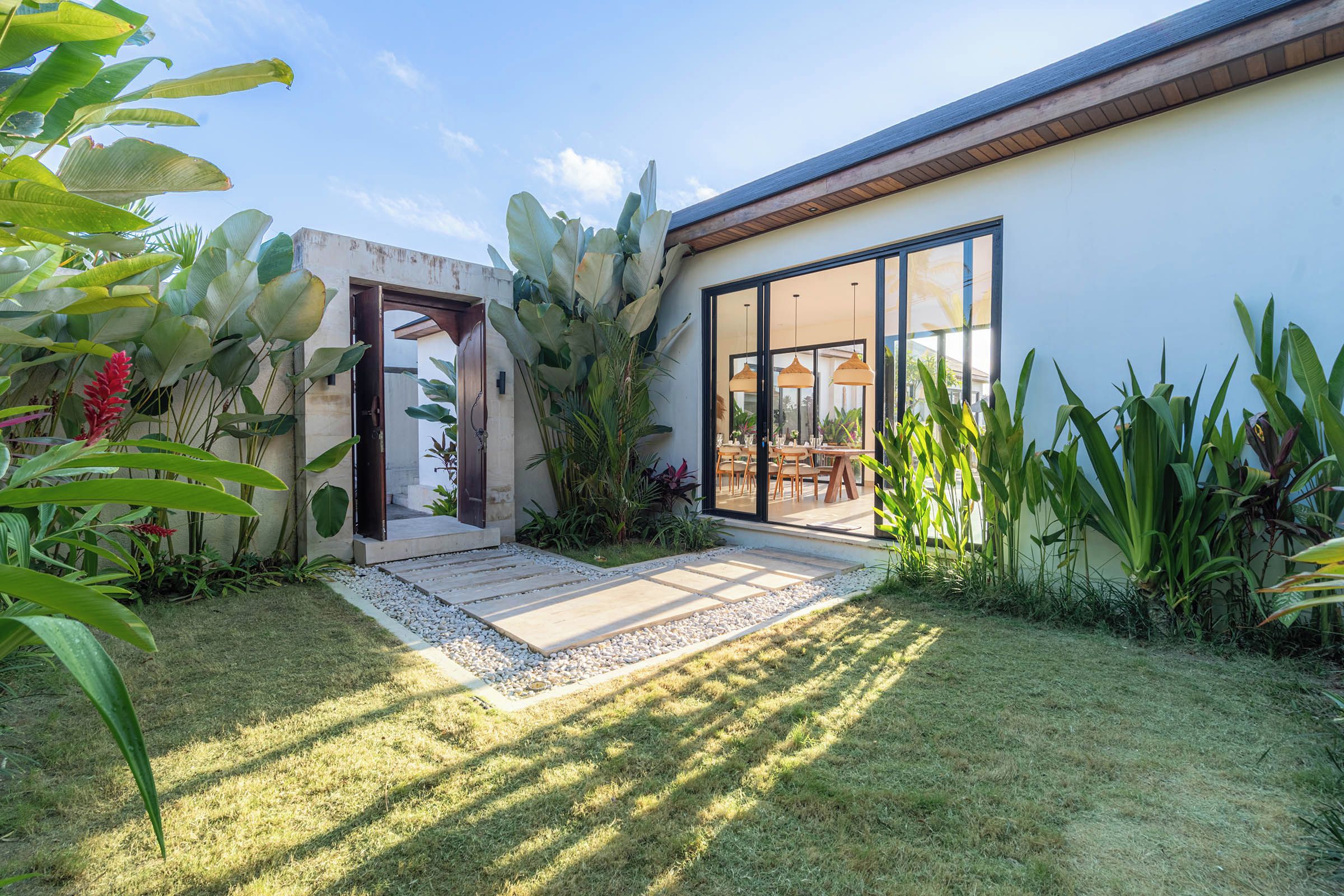 A modern house with a patio, large windows, and tropical plants.