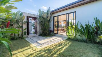 A modern house with a patio, large windows, and tropical plants.