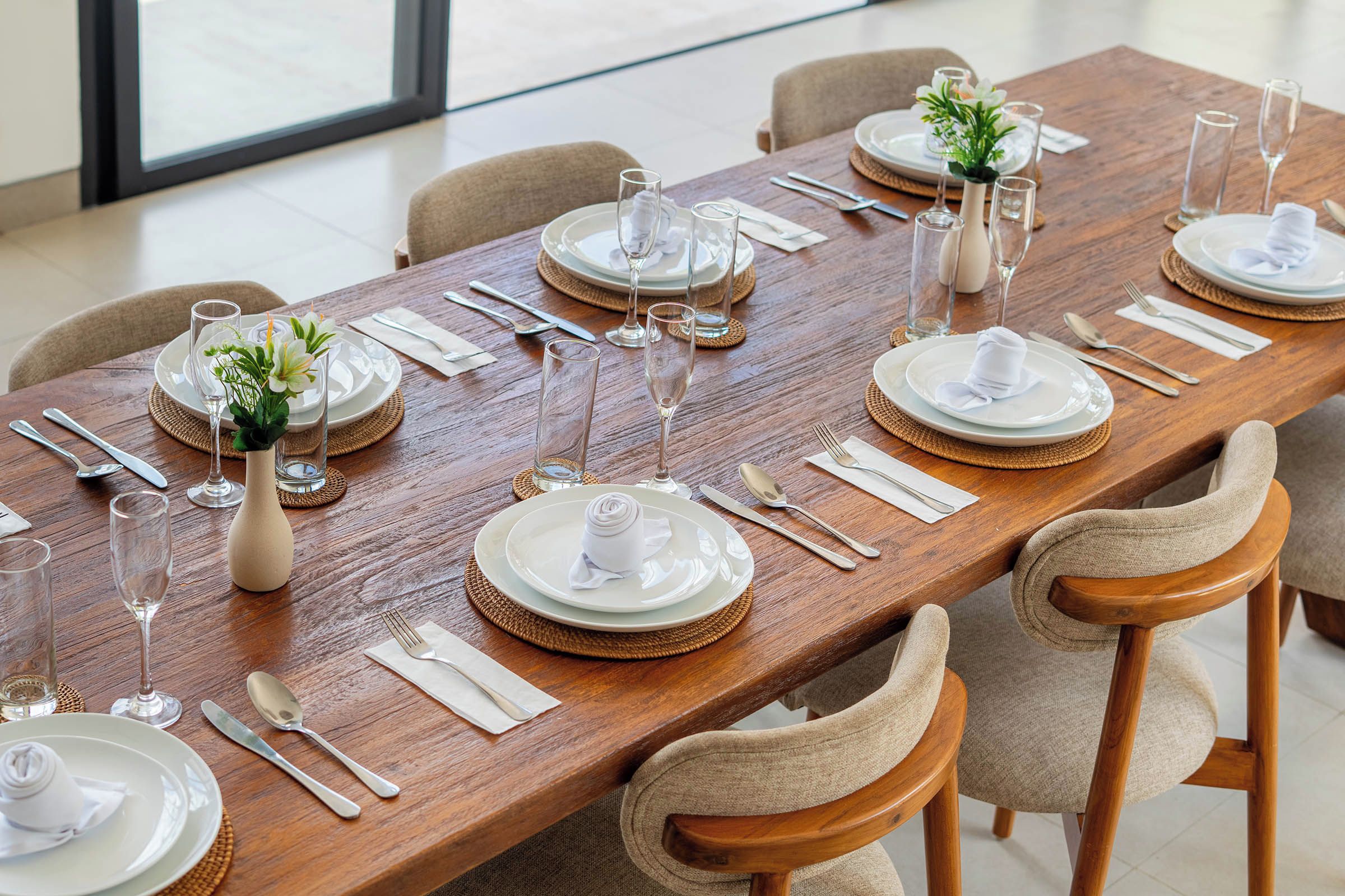 A long dining table set for a meal with multiple chairs, glassware, and white plates.