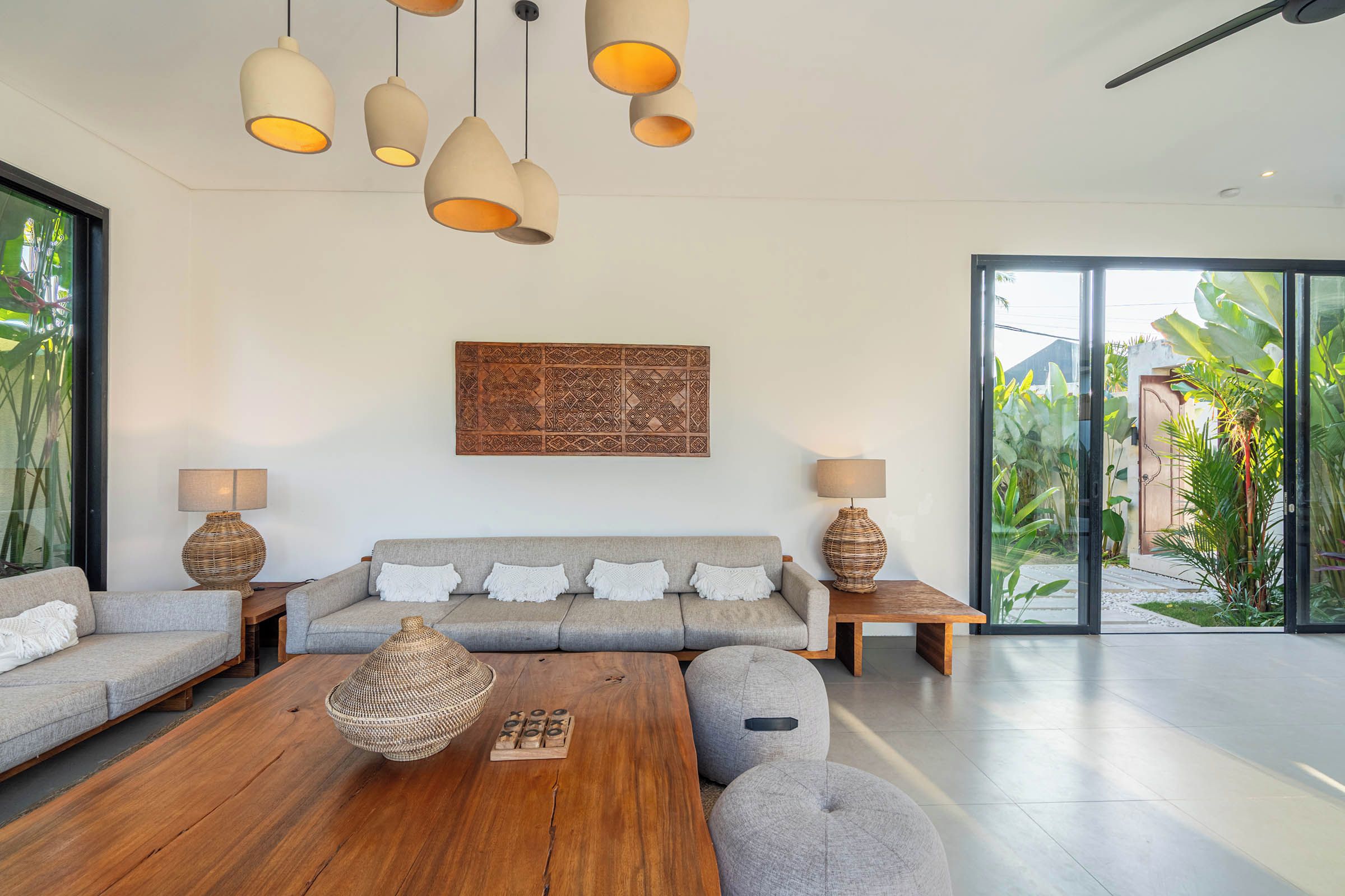 A modern living room with a grey sofa, wooden coffee table, and woven lamps.