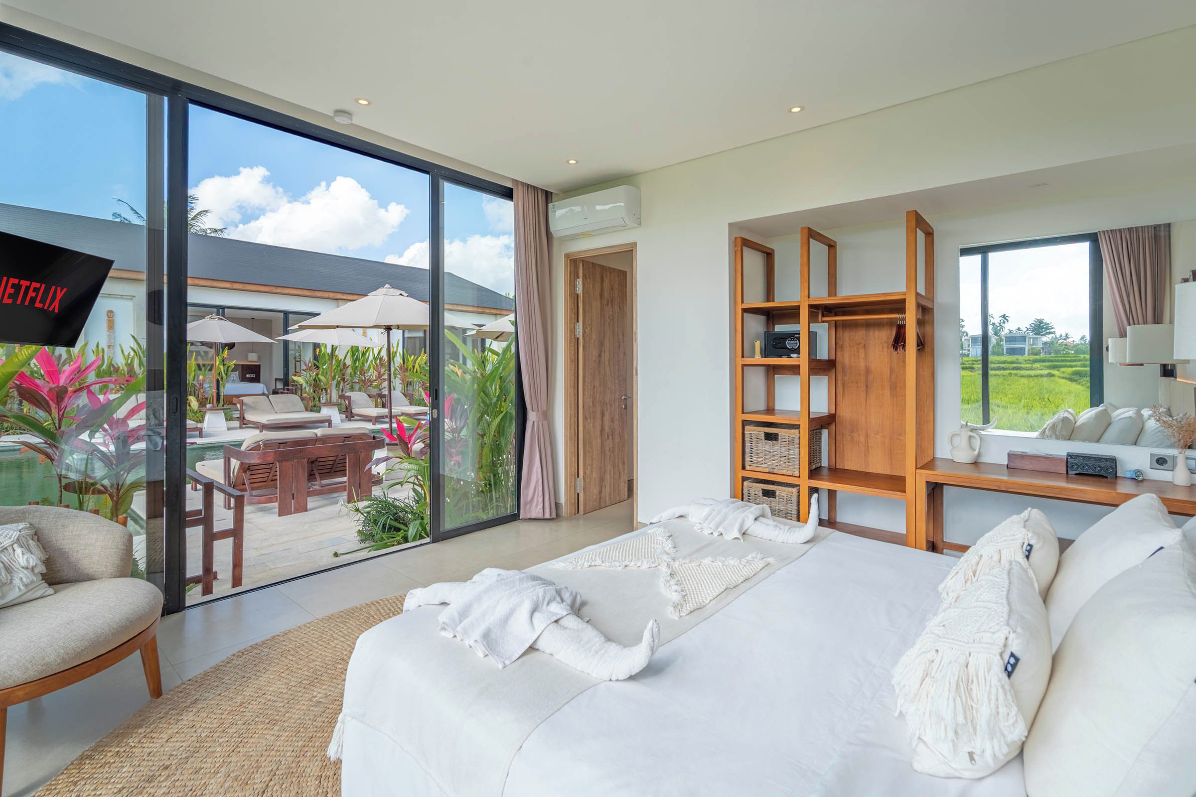 Ein modernes Hotelzimmer mit einem großen Bett, einem Fernseher, einem Holzregal und Blick ins Freie.