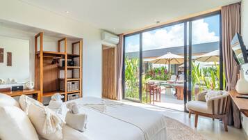A bedroom with a large bed, a wooden wardrobe, a desk with a chair, and a view of an outdoor patio with umbrellas.