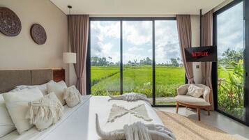 Ein modernes Schlafzimmer mit einem großen Bett, einem Fernseher und Blick auf ein grünes Feld.