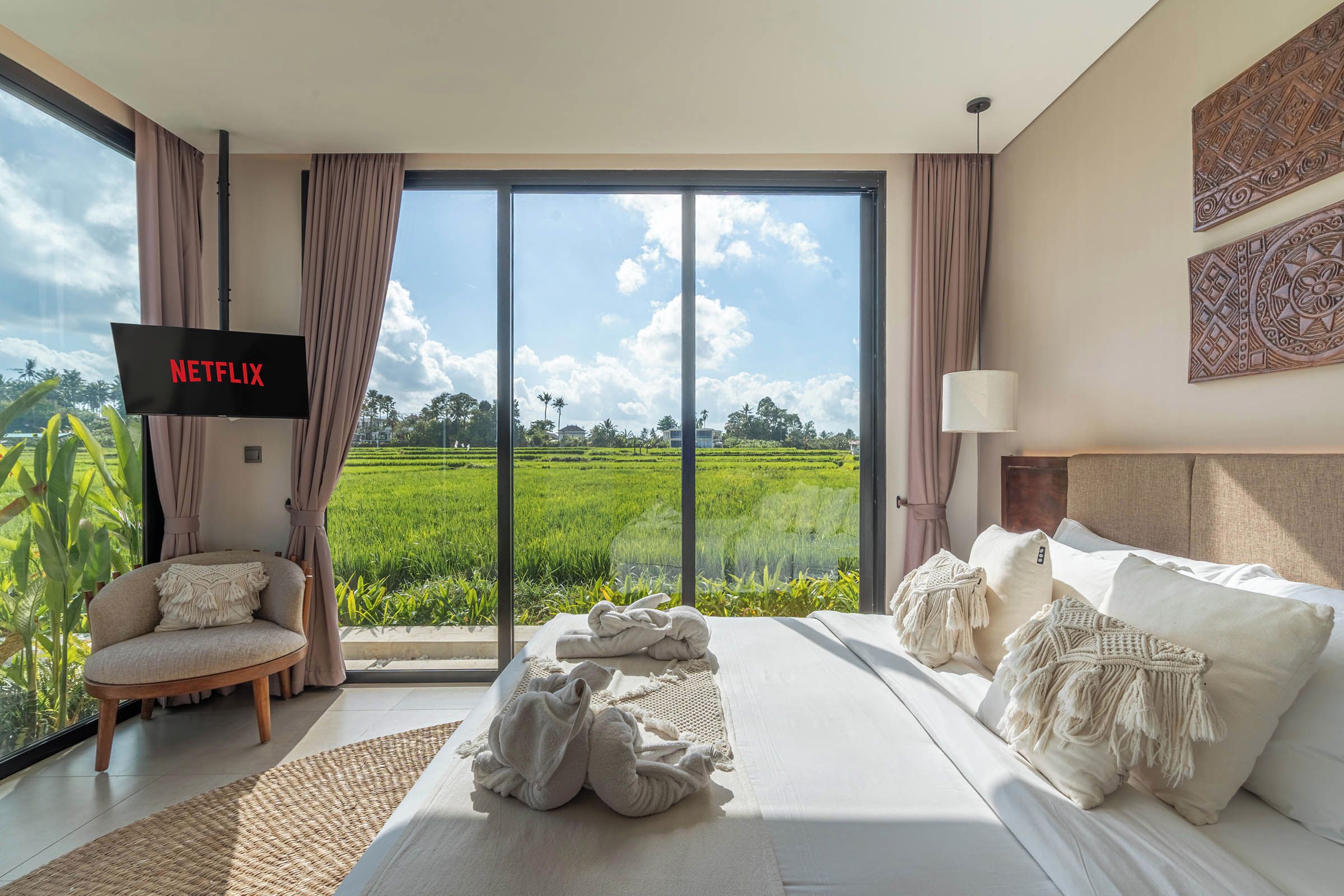 A hotel room with a large window, a bed, a chair, and a TV displaying Netflix.