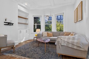 Ein modernes Wohnzimmer mit Sofa, Sessel, Couchtisch und einem gemusterten Teppich.