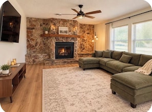 A living room with a stone fireplace, a green sofa, a wooden coffee table, and a ceiling fan. - 3-bedroom 2 full bathroom house in adorable Abilene with cool AC comfort (Abilene)