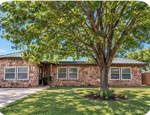 A stone house with a metal roof, a front porch, and a well-maintained lawn. - 3-bedroom 2 full bathroom house in adorable Abilene with cool AC comfort (Abilene)