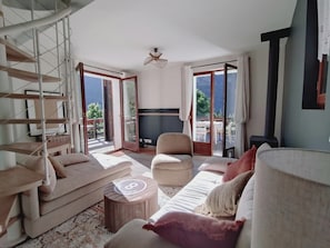 A spacious living room with a sofa, armchair, and a round wooden table. A spiral staircase is visible on the left. - Welcome to Skimoon! Our family chalet with panoramic view of Haut Verdon valley (Villars-Colmars)