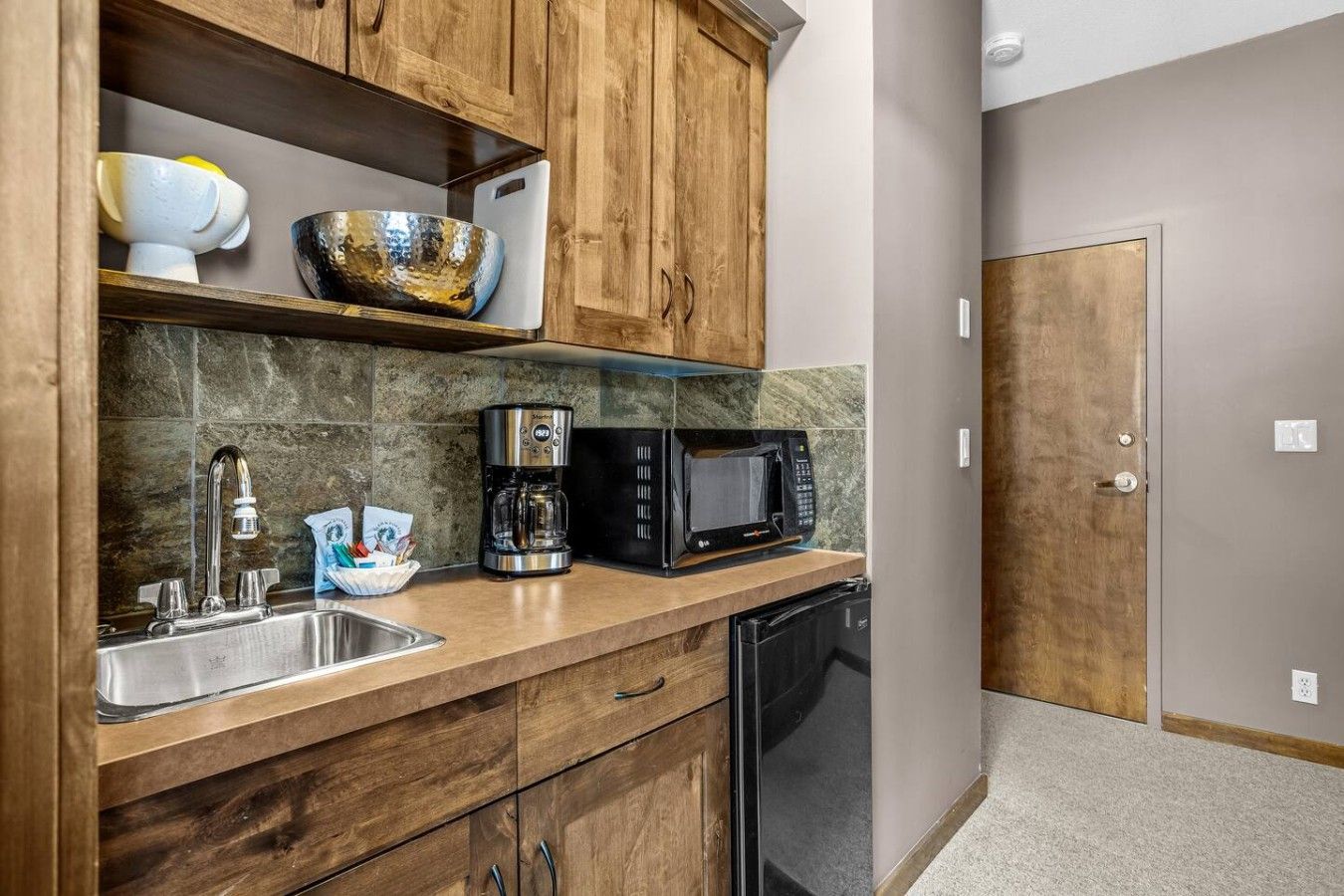 Een compacte keuken met houten kastjes, een koffiezetapparaat, een magnetron en een vaatwasser.
