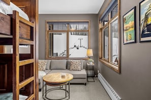 A cozy room with a sofa, a round table, and a window with a view of a snowy landscape. - Elevated Alpine Nest Sleeps 4 Hot tub + Gym! (Golden)