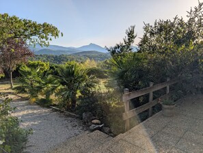 A gravel pathway leading to a wooden bridge over a body of water, surrounded by lush greenery and a mountainous backdrop. - Figarol Cabin (Ground Floor - Pic de Paloumère) (Figarol)