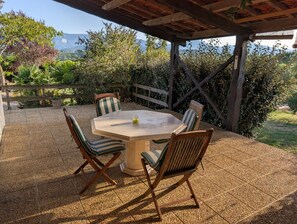 An outdoor patio with a round table and four chairs, surrounded by a wooden fence and various plants. - Figarol Cabin (Ground Floor - Pic de Paloumère) (Figarol)