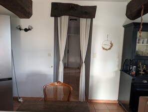 A kitchen with a wooden ceiling, a dining area with a chair, and a doorway leading to another room. - Figarol Cabin (Ground Floor - Pic de Paloumère) (Figarol)