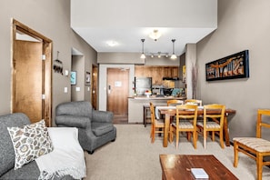 A living room with a gray sofa, a coffee table, and a dining area with wooden chairs and a table. - Kicking Horse 1BR+Loft Hot Tub & Ski-in/Ski-out (Golden)