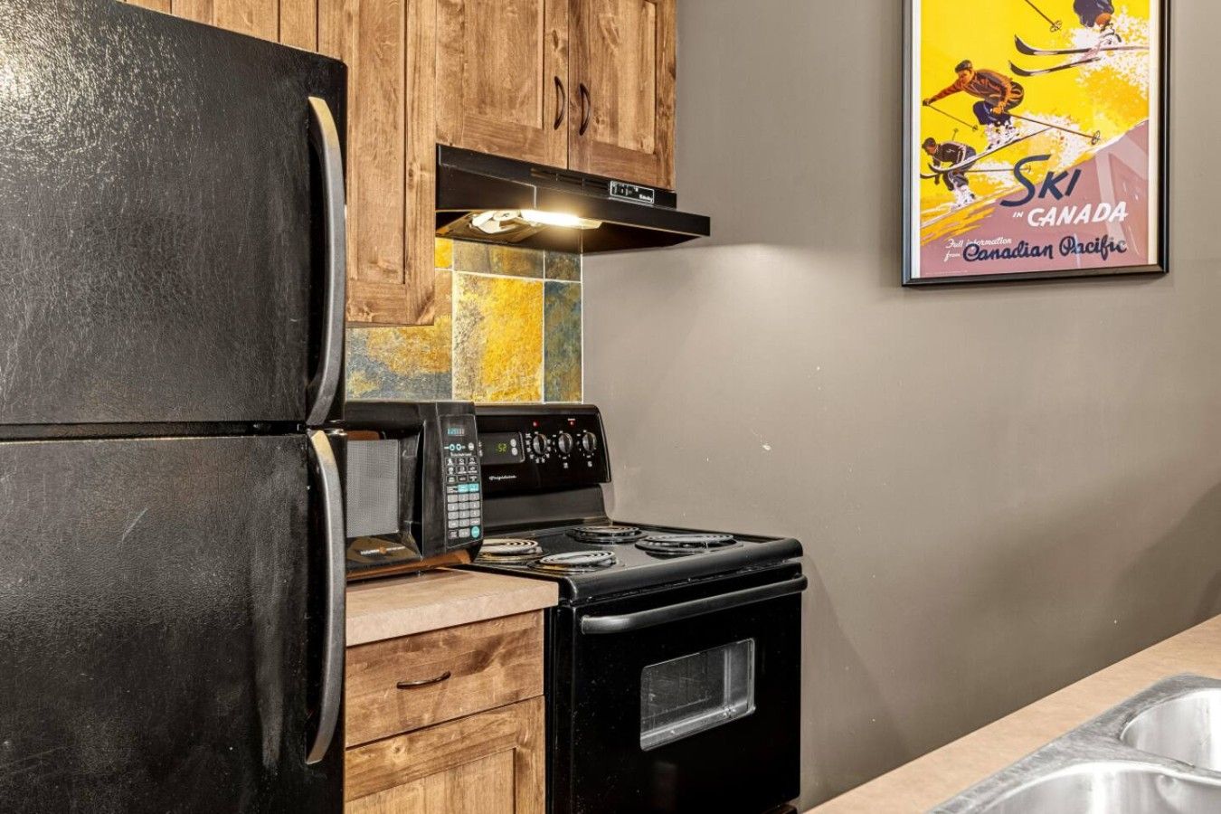 A kitchen with a black refrigerator, a stove, and wooden cabinets.