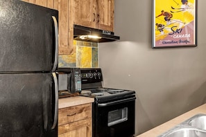 A kitchen with a black refrigerator, a stove, and wooden cabinets. - Kicking Horse 1BR+Loft Hot Tub & Ski-in/Ski-out (Golden)