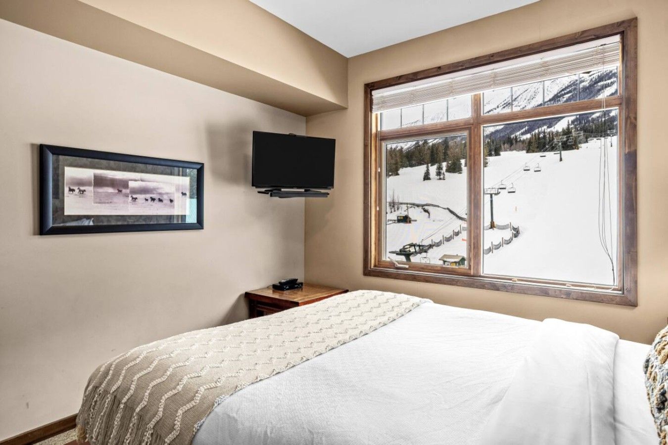 Un dormitorio con una ventana grande, una cama, un televisor de pantalla plana y una fotografía enmarcada en la pared.