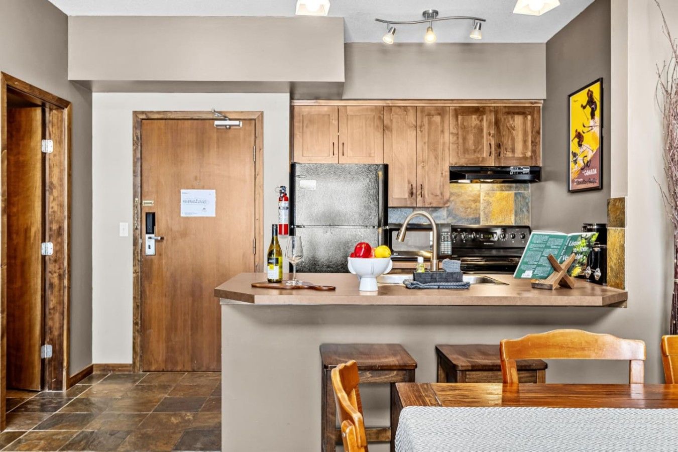 Una cocina moderna con armarios de madera, un refrigerador integrado y una zona de comedor con mesa y sillas.