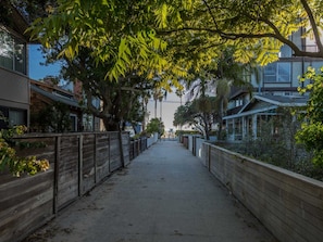 A tree-lined pathway between residential buildings with a clear sky above. - Venice Beach House (Los Angeles)
