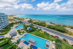 Ein Resort mit mehreren Swimmingpools, einer Strandpromenade und einer Straße, die parallel zum Strand verläuft.