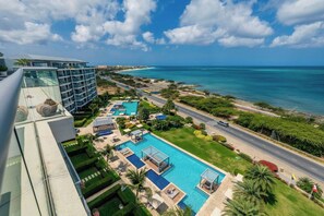 Ein Resort mit einem großen Schwimmbad, Blick auf den Ozean und einer parallel zum Pool verlaufenden Straße.