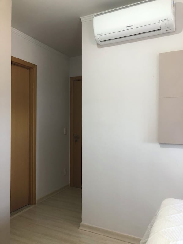 A room with a white air conditioning unit mounted on the wall, a wooden door, and a white wall.