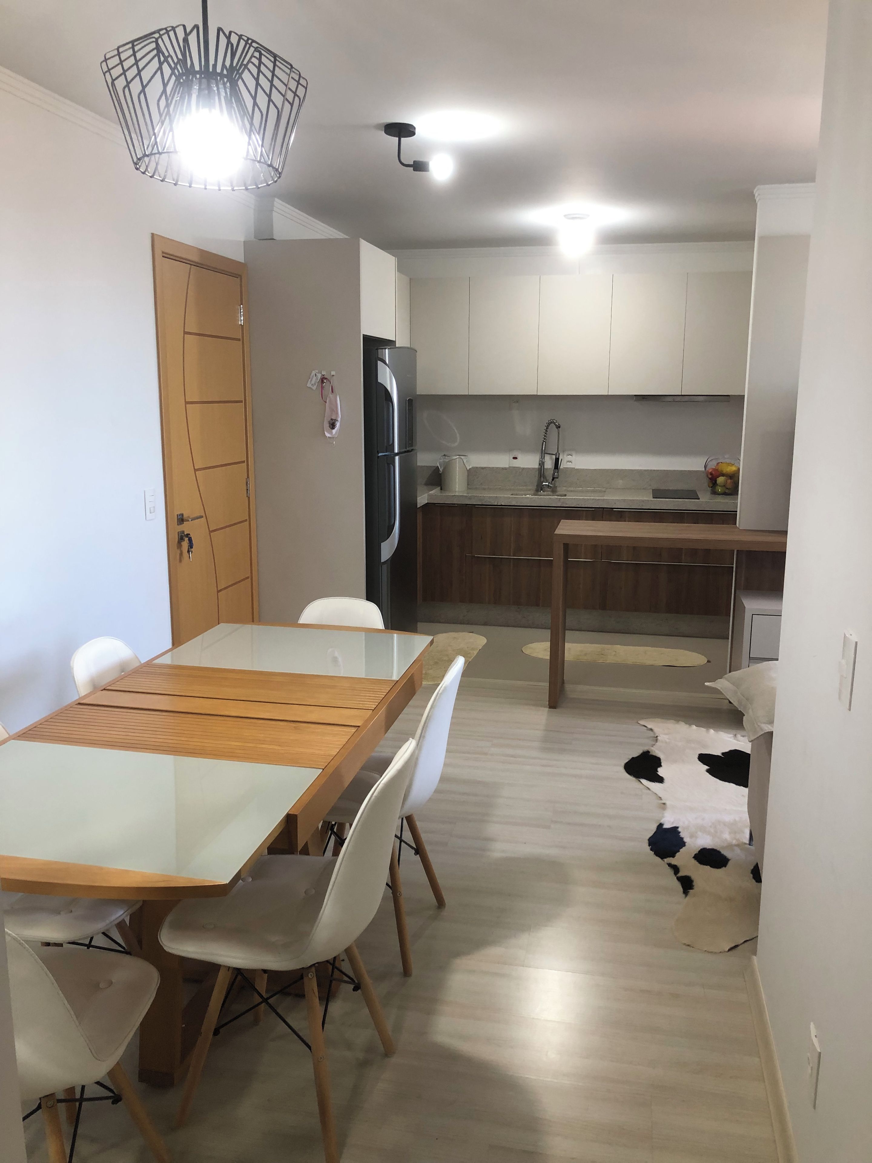 A modern kitchen with white cabinets, a stainless steel refrigerator, and a dining area with a wooden table and white chairs.
