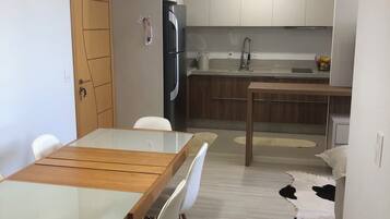 A modern kitchen with white cabinets, a stainless steel refrigerator, and a dining area with a wooden table and white chairs.