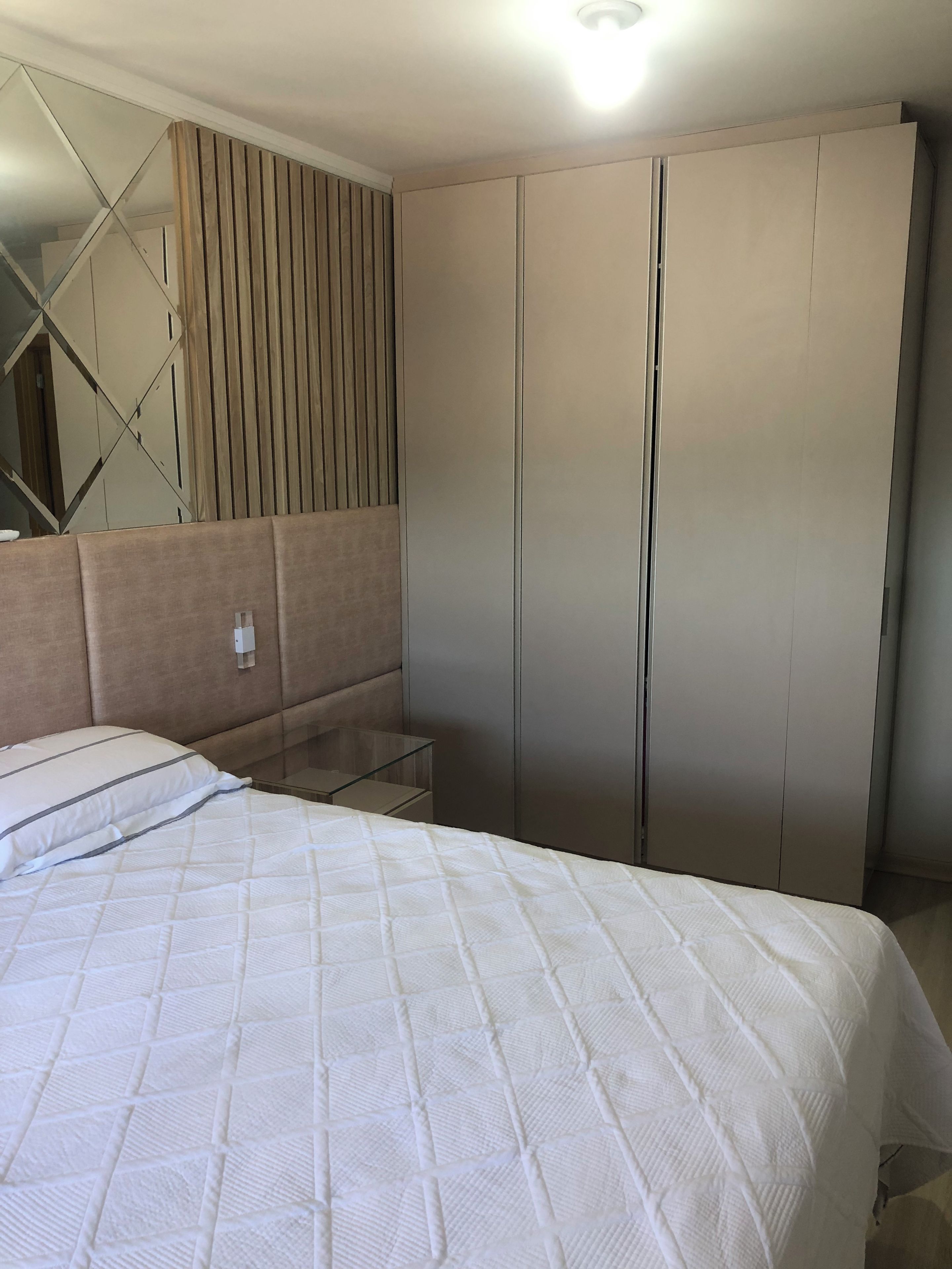 A bedroom with a bed, a bedside table, a mirror, and a wardrobe.