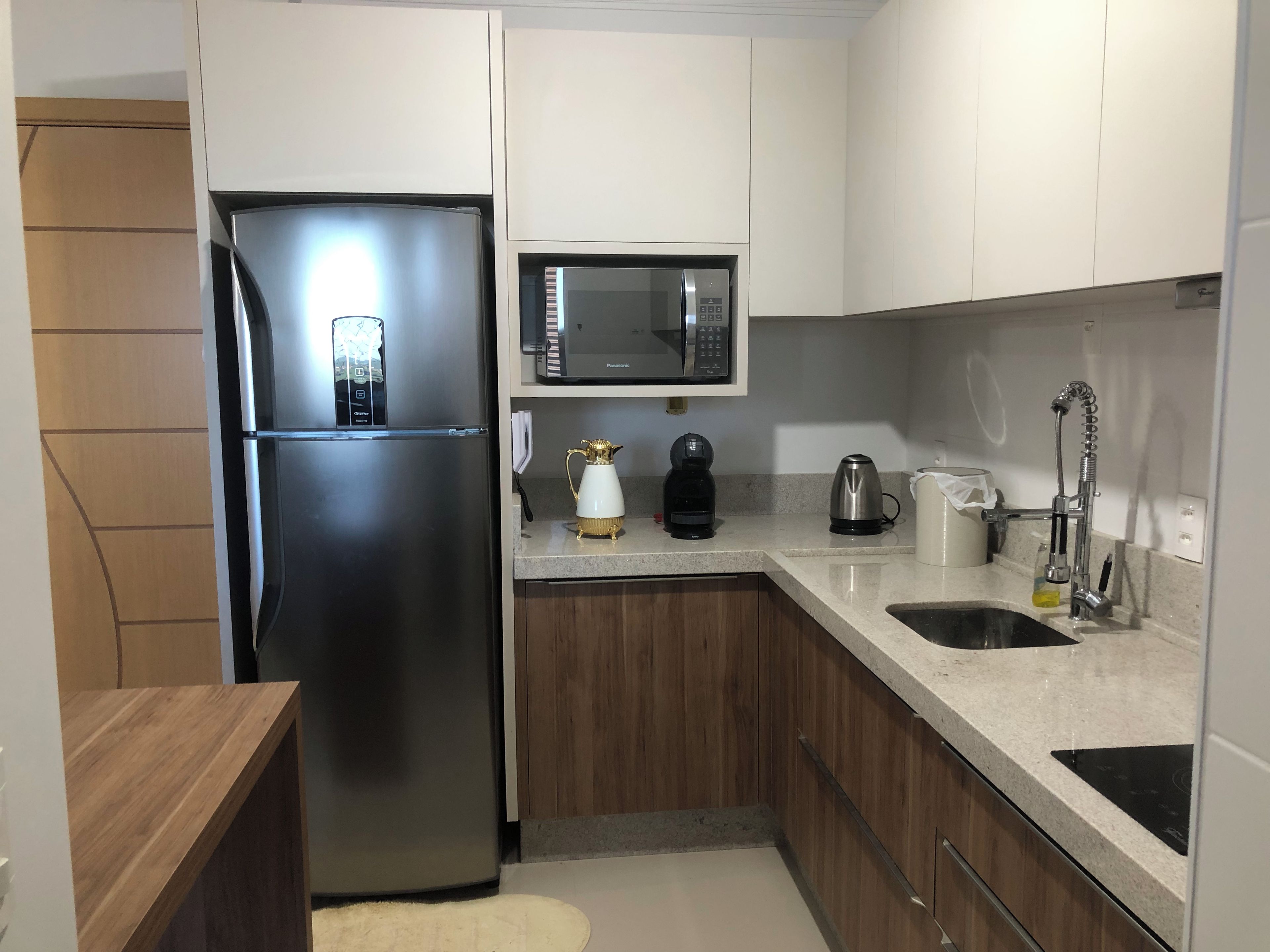 A compact kitchen with a stainless steel refrigerator, a microwave, a coffee maker, and a sink.
