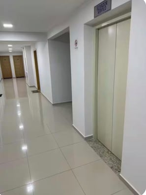 A clean, well-lit hallway with a sign indicating elevator service, a tiled floor, and a door with a no-smoking sign.