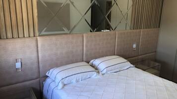 A hotel room with a bed, a nightstand, a mirror, and a wall-mounted air conditioning unit.