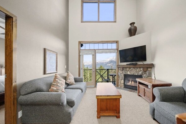 Ein Wohnzimmer mit Kamin, Fernseher und Bergblick durch große Fenster.