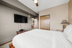 Ein Hotelzimmer mit einem großen Bett, einem wandmontierten Flachbildfernseher, einem Nachttisch aus Holz, einer Lampe und einer Tür zu einem Badezimmer.