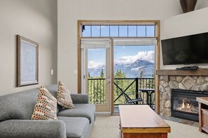Ein Wohnzimmer mit grauem Sofa, gemusterten Kissen, einem Holztisch, einem Kamin aus Stein und einem Fernseher.