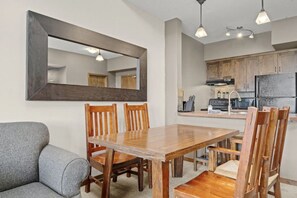 A dining area with a wooden table and chairs, a grey sofa, and a kitchen in the background. - Golden Peak Retreat 1BR+Loft Ski-in/out! (Golden)