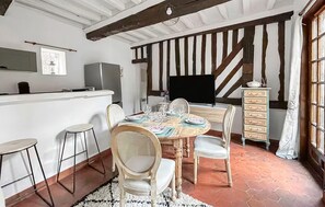 A dining area with a wooden table set for four, surrounded by chairs, a television, and a cabinet with drawers. - Lovely apartment in Pont-Audemer with WiFi (Pont-Audemer)
