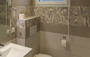 Ein Badezimmer mit Toilette, Waschbecken und Spiegel. An der Wand befinden sich zwei Toilettenpapierrollen.